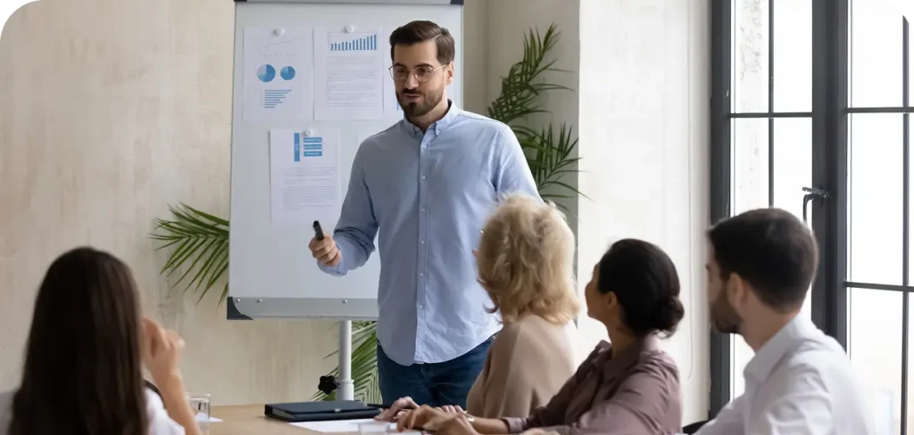 confident-handsome-businessman-flip-charts-presentation-new-project-boardroom-company-meeting-happy-coach-auditor-speaks-with-diverse-colleagues-about-business-using-board-graphs